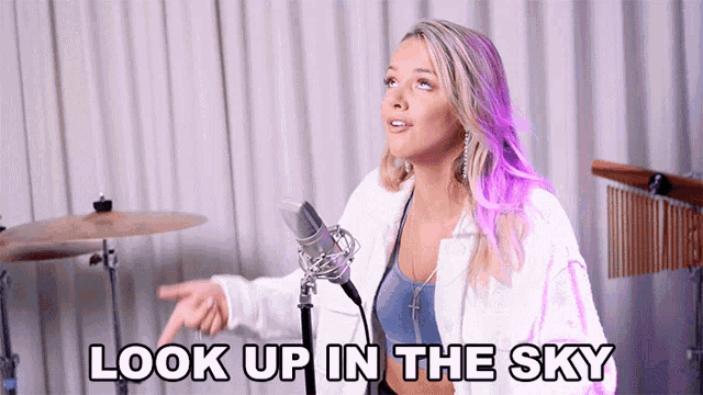 a woman standing in front of a microphone with the words look up in the sky above her