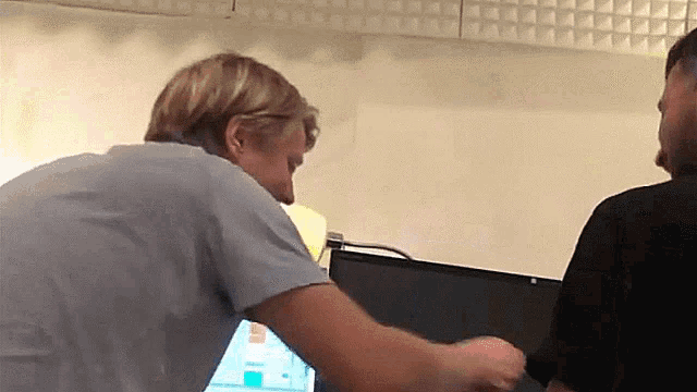a man in a blue shirt is talking to another man in a black shirt in front of a computer monitor