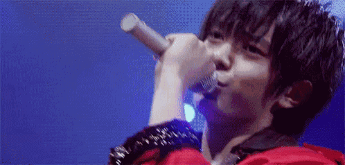 a young man in a red jacket is singing into a microphone on a stage .