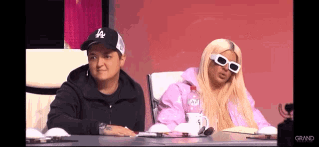 a man in a la hat sits next to a woman in sunglasses