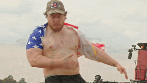 a shirtless man wearing a camo hat is standing in front of an american flag