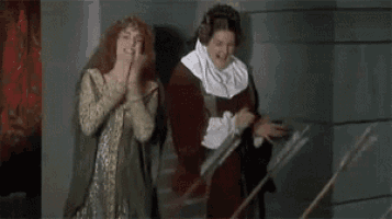two women in medieval costumes are clapping while standing next to each other .