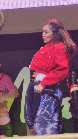 a woman in a red jacket is holding a microphone in front of a sign that says m