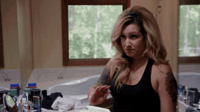a woman in a black tank top looks at herself in a mirror