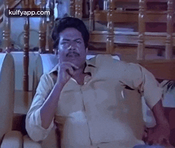 a man is sitting on a couch with his hand on his chin and making a funny face .