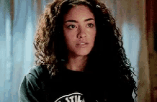 a woman with curly hair is wearing a black t-shirt with a logo on it .