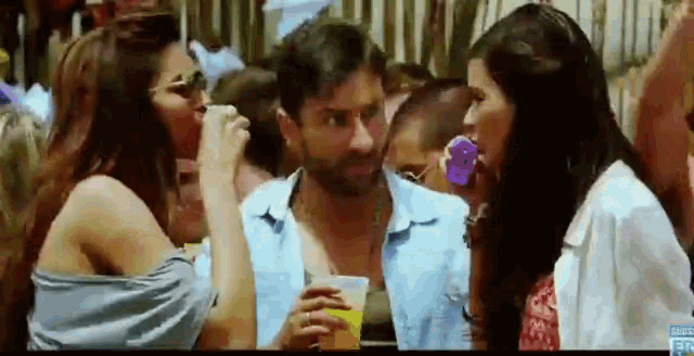 a man and two women are sitting at a table with a drink in their hand .