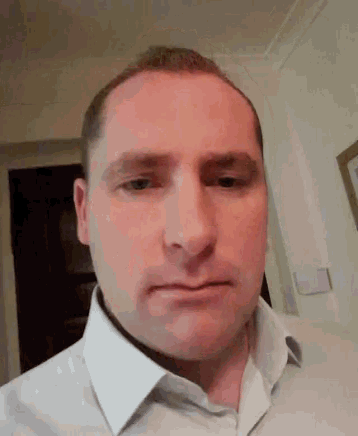 a man in a white shirt is making a funny face while looking at the camera .