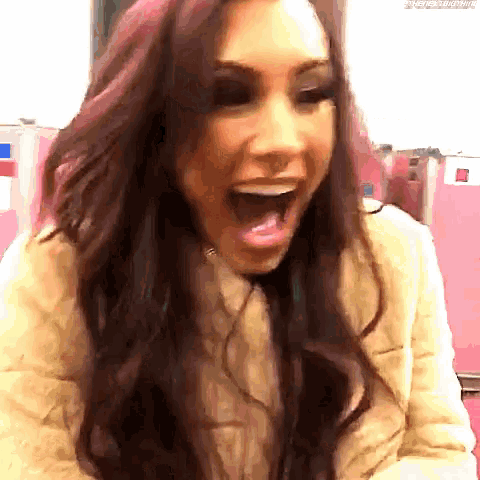 a woman with long red hair is laughing with her mouth open and wearing a tan jacket .