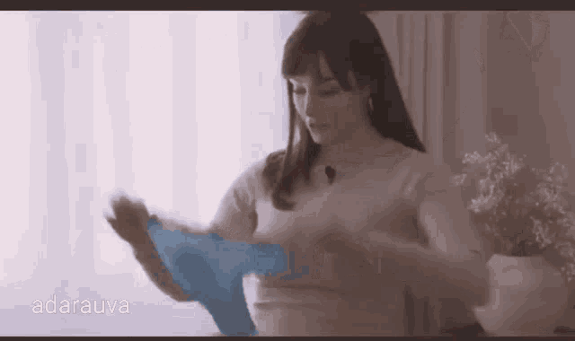 a woman is standing in front of a window holding a blue sweater .