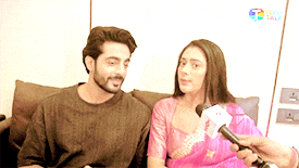 a man and woman are sitting on a couch being interviewed by a reporter