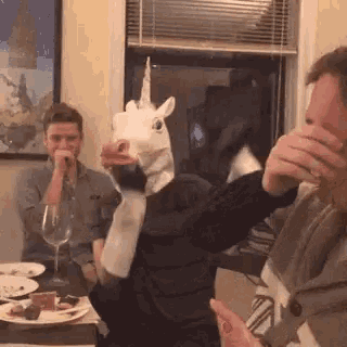 a man wearing a unicorn mask is sitting at a table .
