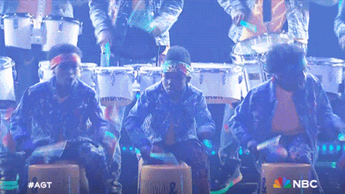 a group of people playing drums on a stage with the nbc logo in the background