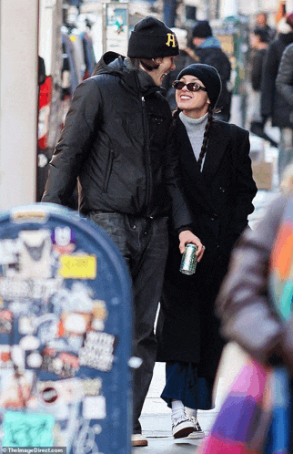 a man wearing a beanie with the letter h on it is holding a woman 's hand