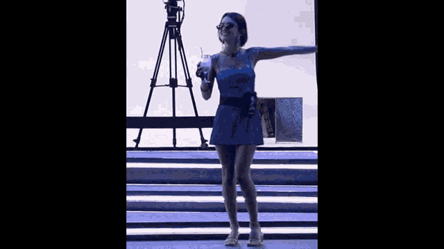 a woman in a blue dress is standing on a stage holding a drink
