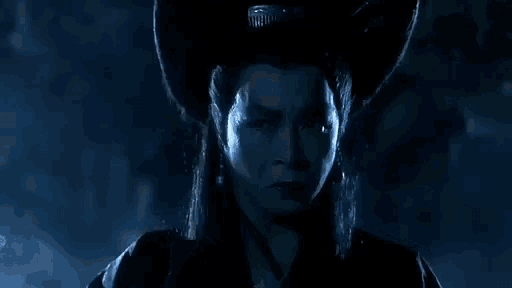 a woman wearing a cowboy hat and earrings is smoking a cigarette in the dark .