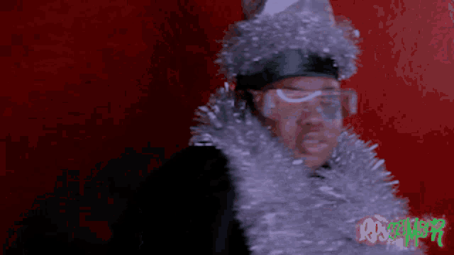a man wearing a santa hat and a tinsel around his neck with the word christmas on the bottom right
