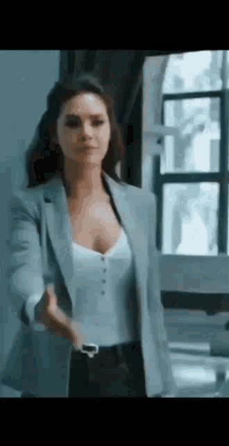 a woman is standing in front of a window wearing a blazer and a white top .