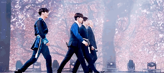a group of men are walking on a stage in front of a tree with flowers .