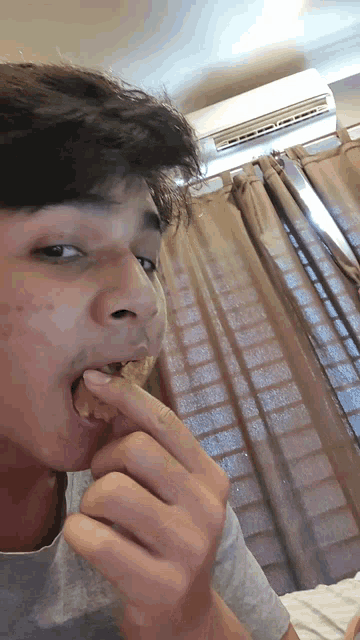 a young man eating a piece of food in front of a window