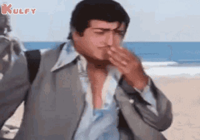 a man in a suit is standing on a beach covering his nose .