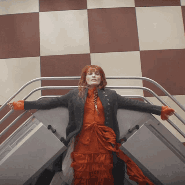 a woman in an orange dress is standing on a staircase with her arms outstretched