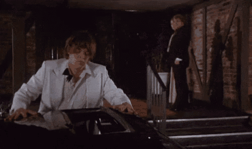 a man in a white suit is standing in front of a black car .