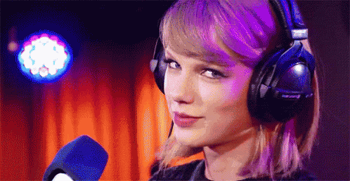 taylor swift is wearing headphones and talking into a microphone in a dark room .