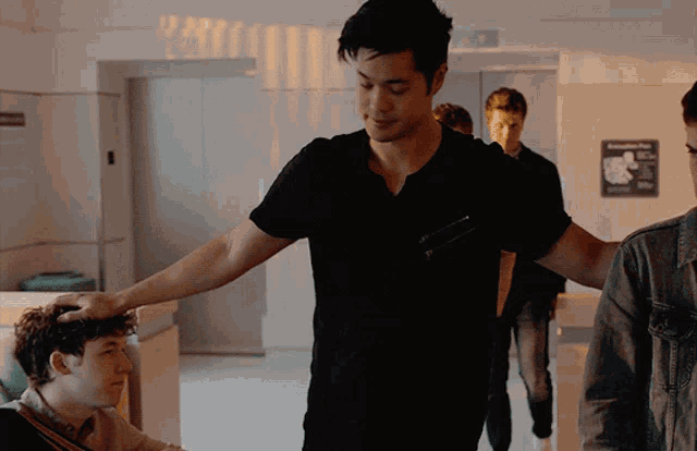 a man in a black shirt has his hand on another man 's head in a hallway