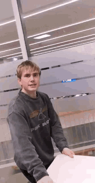 a young man is standing in front of a window wearing a pink floyd sweatshirt .