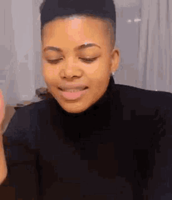a woman with short hair is wearing a black turtleneck and making a funny face with her eyes closed .