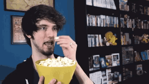 a man eating a bowl of popcorn in front of a bookshelf