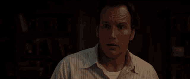a man in a striped shirt is standing in a dark room