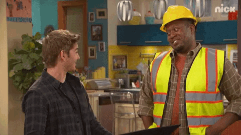 a man wearing a hard hat and safety vest talks to another man in a kitchen .
