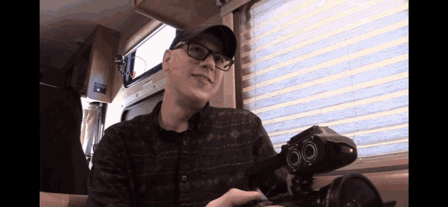 a man wearing glasses and a baseball cap holds a camera