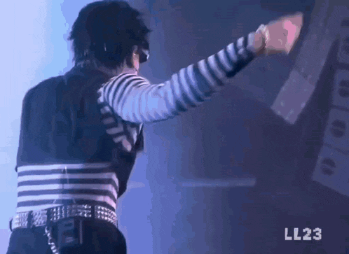 a man wearing a black and white striped shirt is standing on a stage with his arms outstretched .