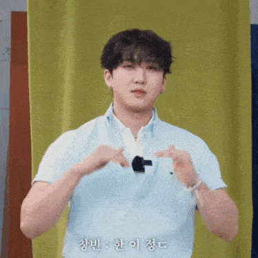 a young man in a blue shirt is making a heart with his hands