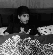 a man in a black shirt is laying in bed with a patterned comforter