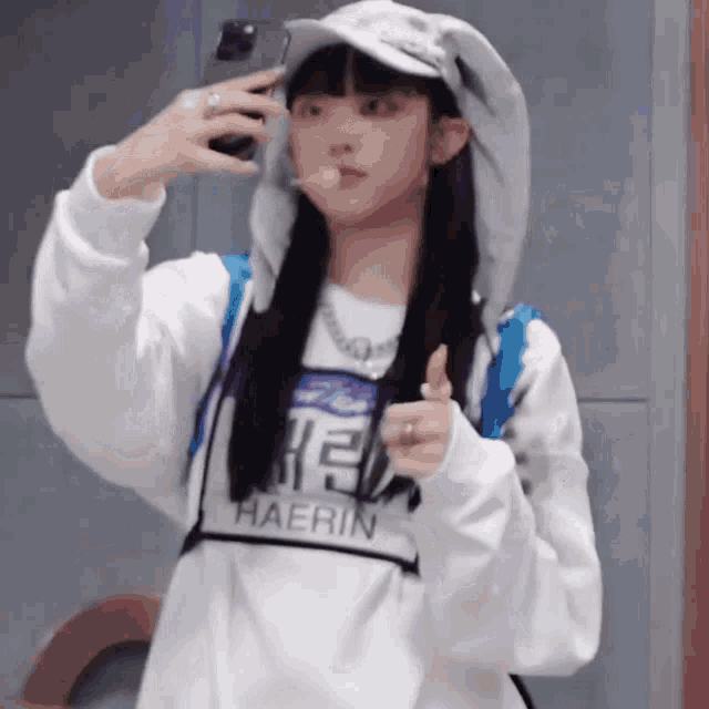 a girl wearing a hoodie and a hat is taking a selfie with her cell phone .