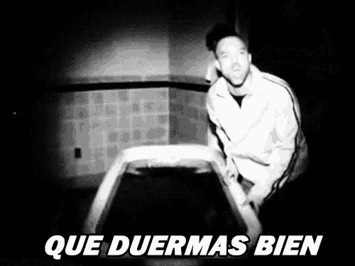 a man is sitting on a bed in a black and white photo with the words `` que duermas bien '' below him .