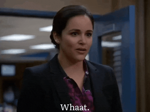 a woman in a suit says " whaat " in front of a blue door