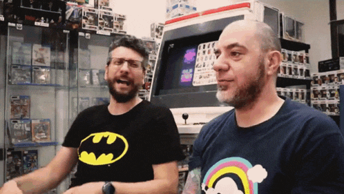 a man wearing a batman shirt is standing next to another man wearing a rainbow shirt