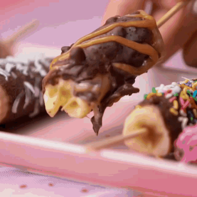 a person is eating a chocolate covered banana on a stick with sprinkles
