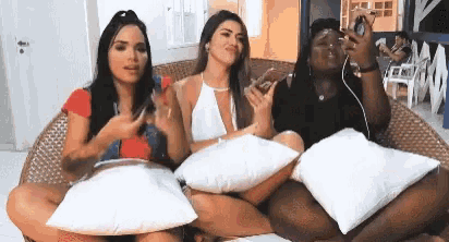 three women are sitting on a wicker chair with pillows .