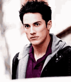 a man wearing a black jacket and a purple shirt looks at the camera