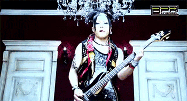 a man is playing a guitar in front of a chandelier with the letters bpr on the bottom