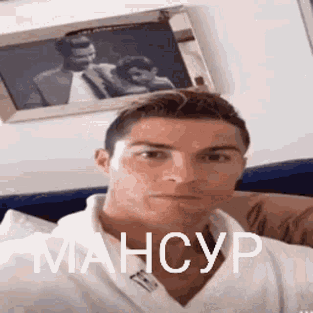 a man in a white shirt is taking a selfie in front of a picture of a man and woman .