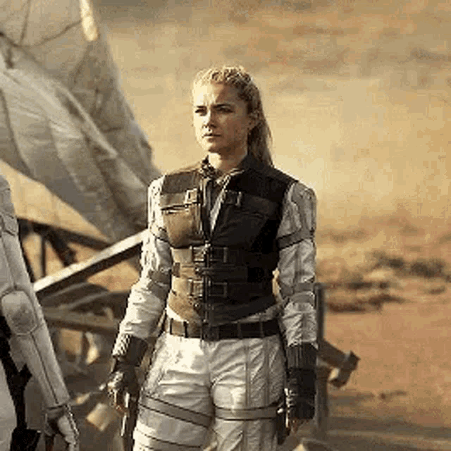 a woman in a military uniform is standing next to a man in a white suit in the desert .