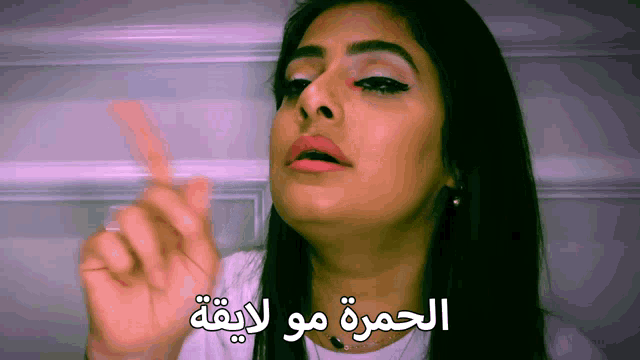 a woman in a white shirt is making a funny face with arabic writing behind her
