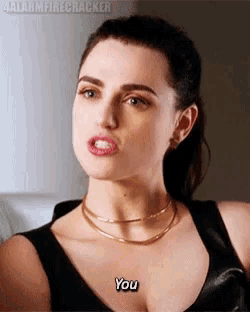 a woman wearing a black tank top and a gold necklace is making a funny face and says `` you '' .
